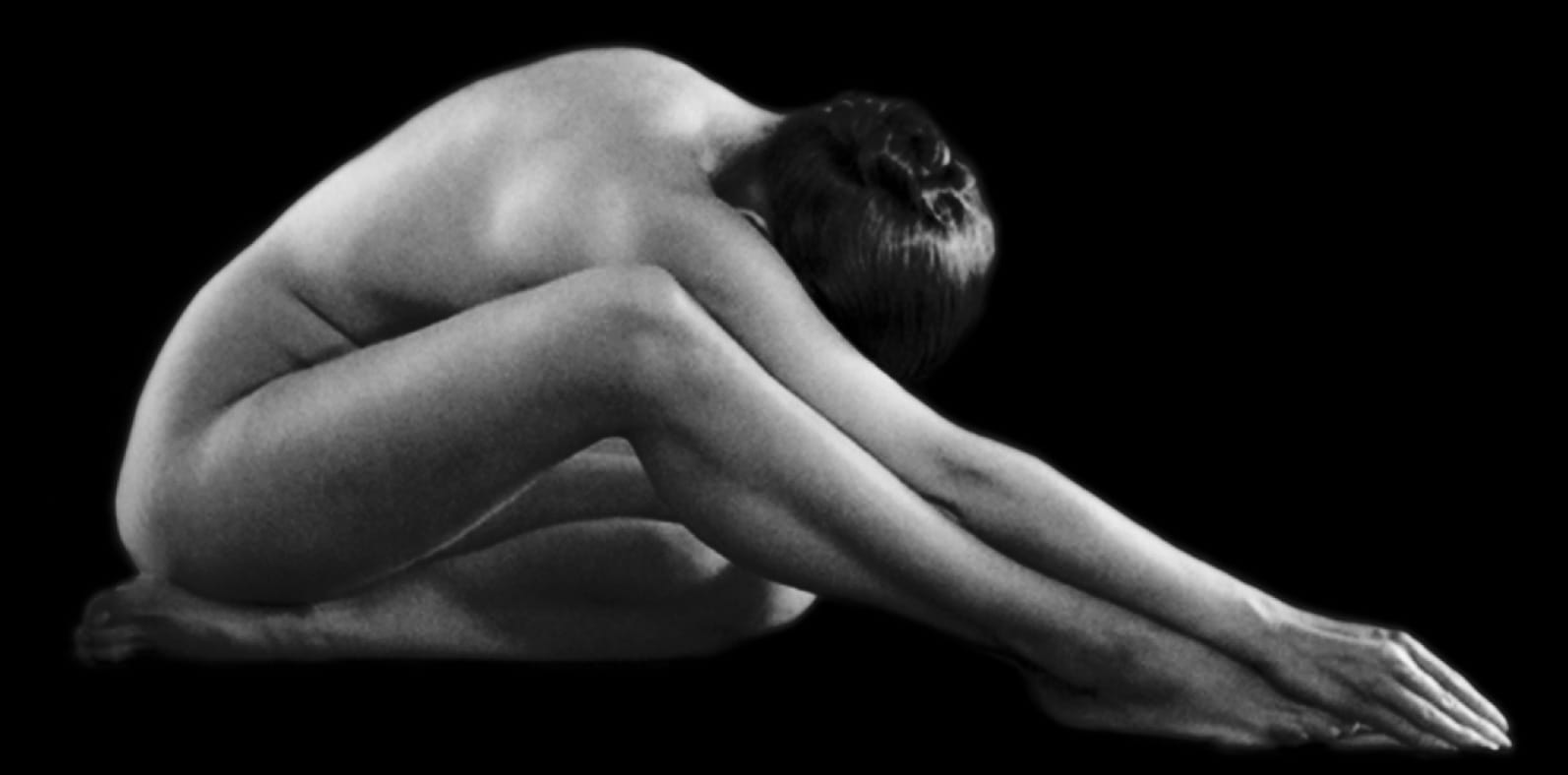 Naked woman sitting down while reaching for her feet with her hands