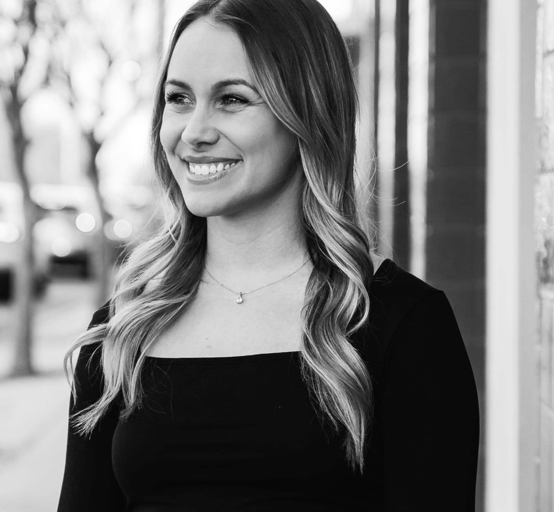 A woman standing on the sidewalk smiling.