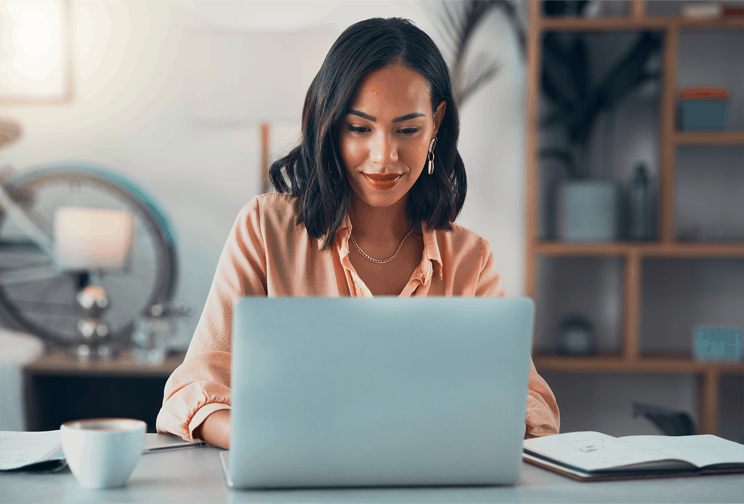 Woman with Short Black Hair and a Light Orange Shirt Looking at her Laptop