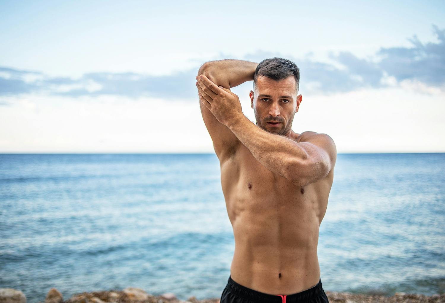 Fit, Shirtless Man Stretching with the Ocean in the Background