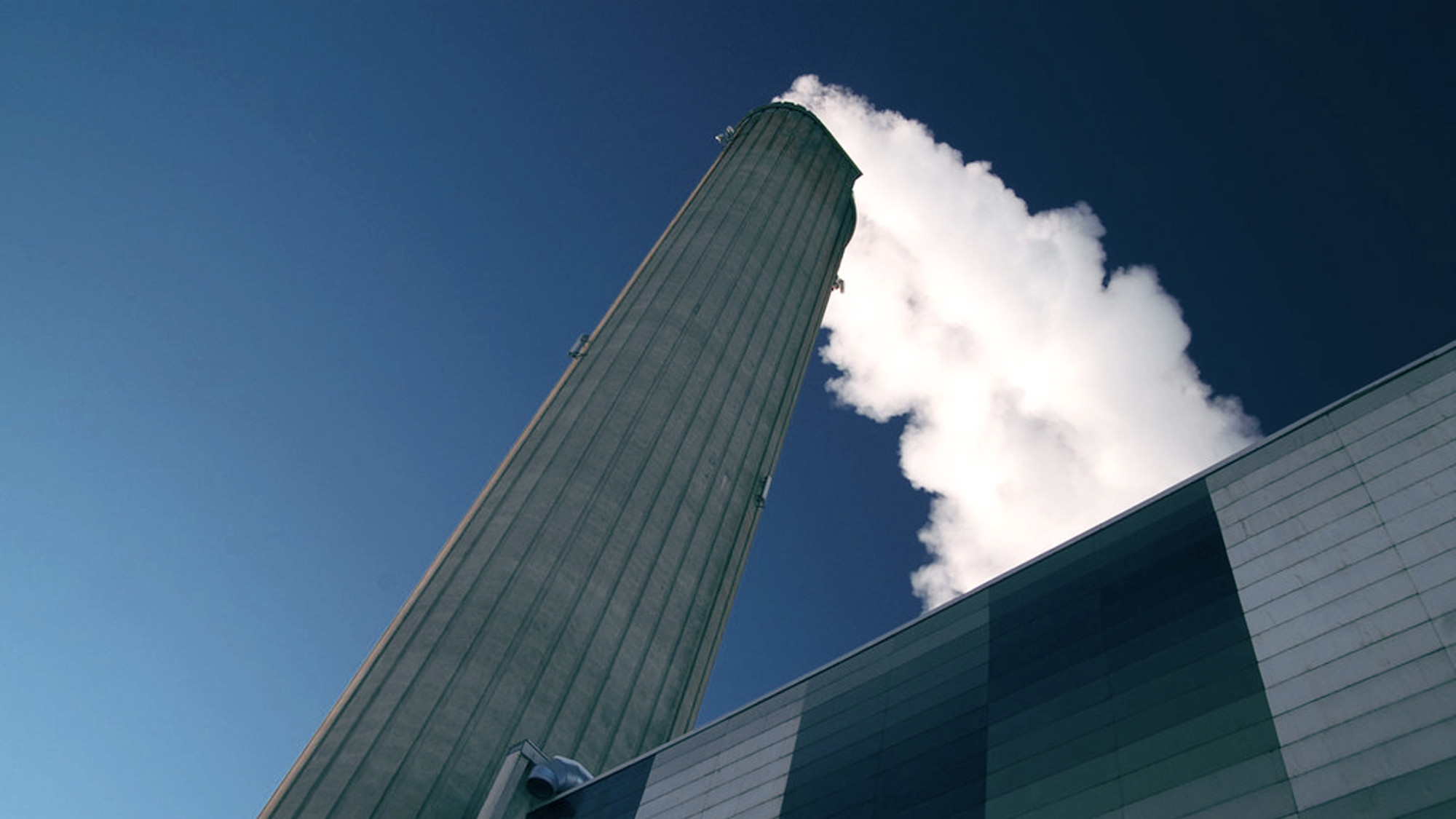 Looking up at power plant chimney emitting steam into deep blue sky