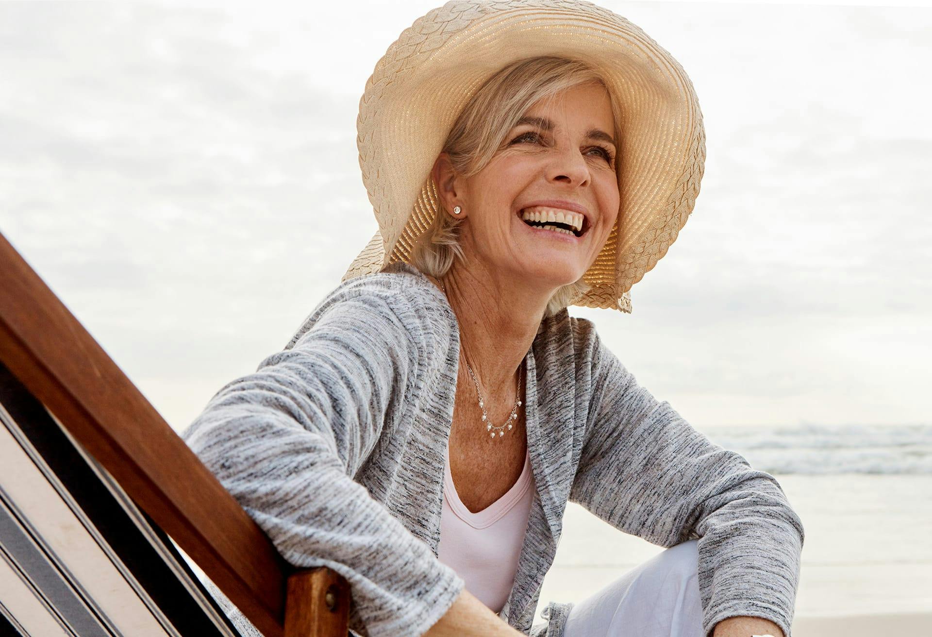 Woman with a hat on next to the ocean, smiling