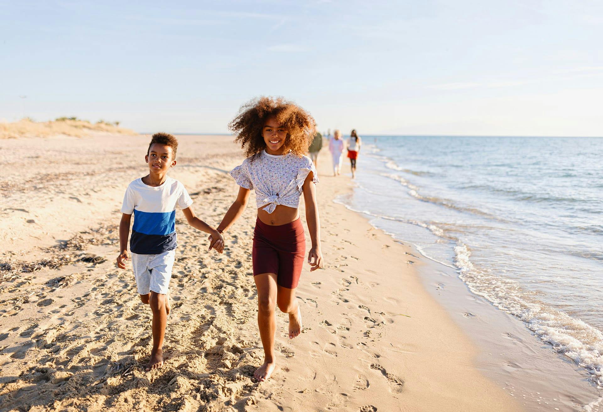 Two kids holding hands and walking on the beach