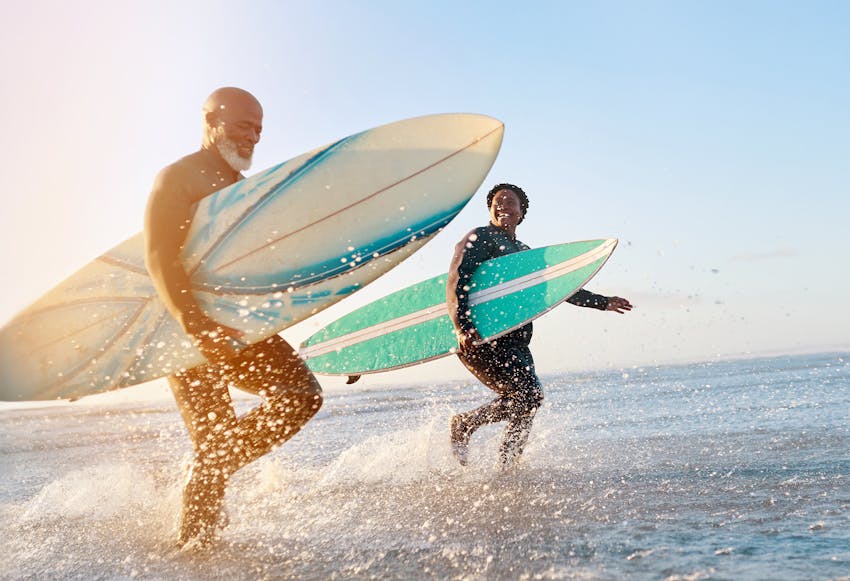 Two people walking in the ocean with surfboards