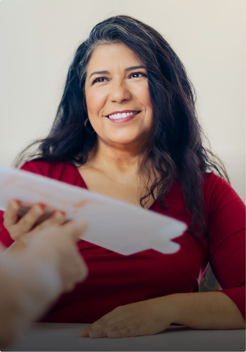 Smiling woman handing papers across a desk.