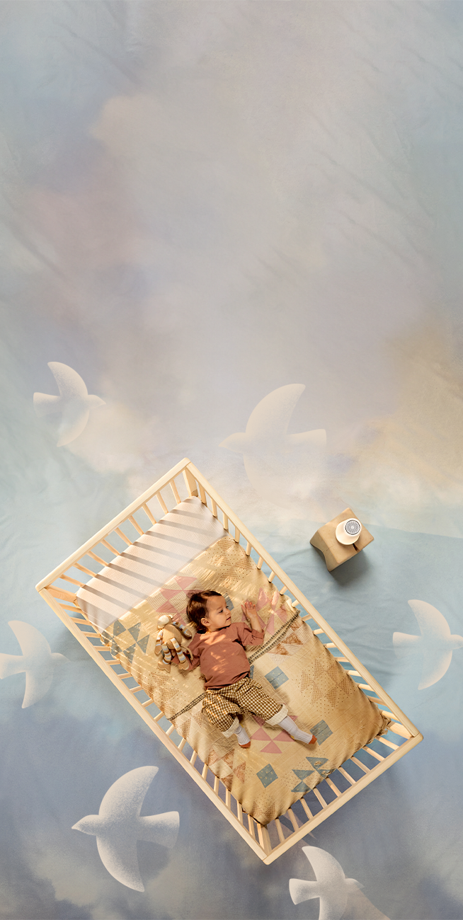 A baby sleeps in a bassinet while listening to their Rest device