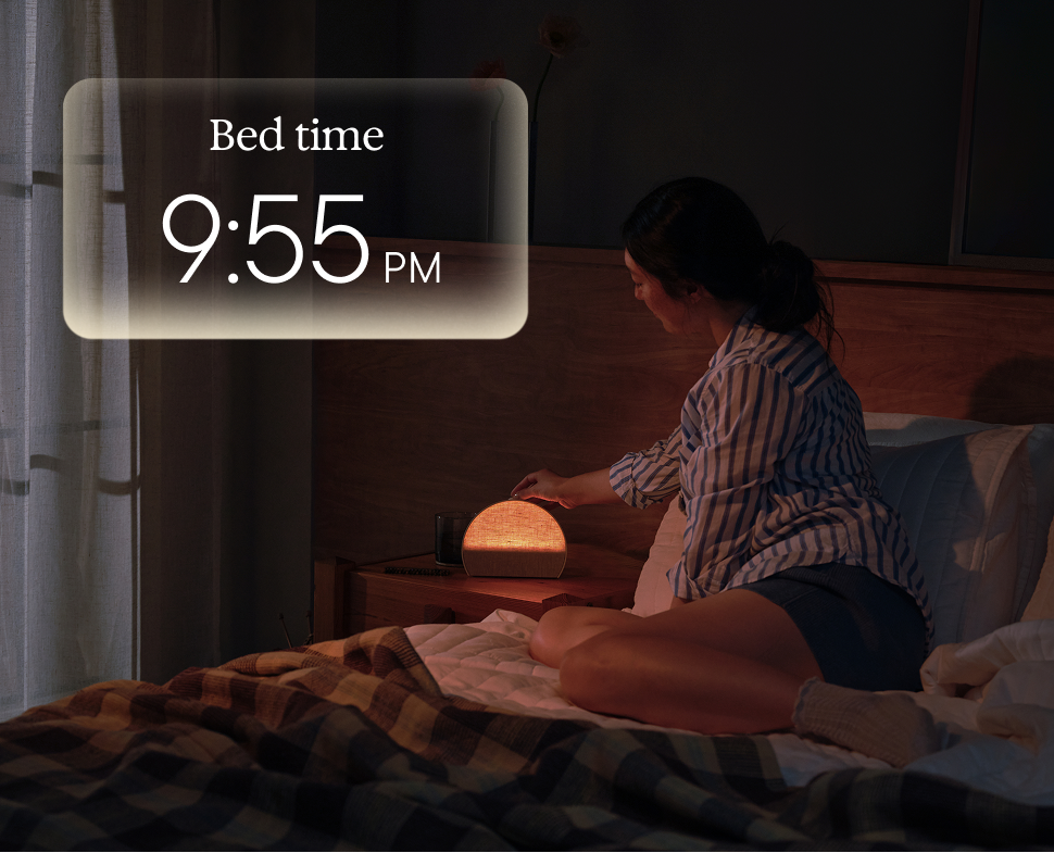 Person reading in bed with a Hatch Sleep Clock on the nightstand