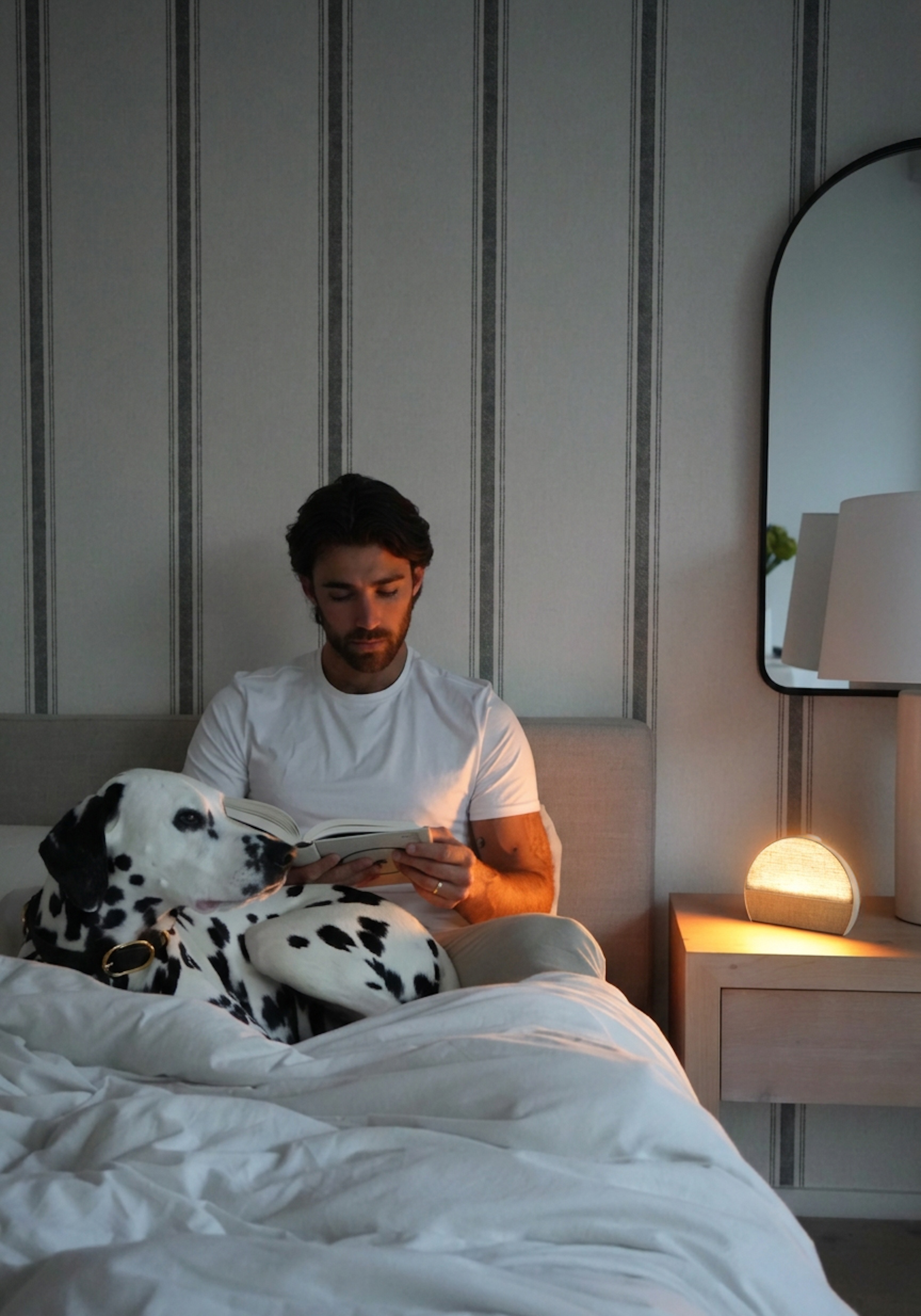 A Hatch Sleep Clock glowing on a wooden nightstand beside a table lamp and a candle