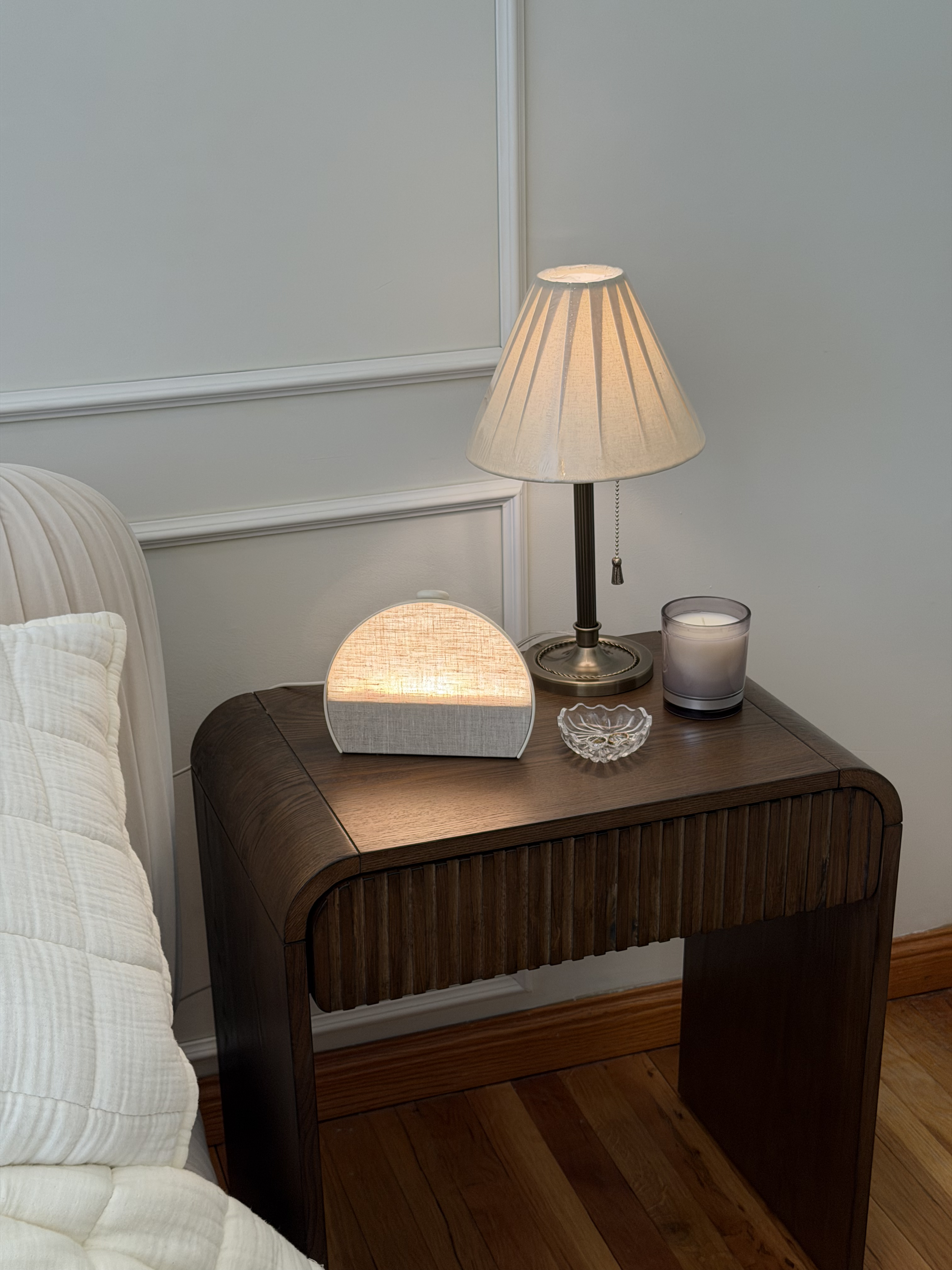 Hands holding a phone showing the Hatch app's sleep details, with a Hatch Sleep Clock glowing on the nightstand behind