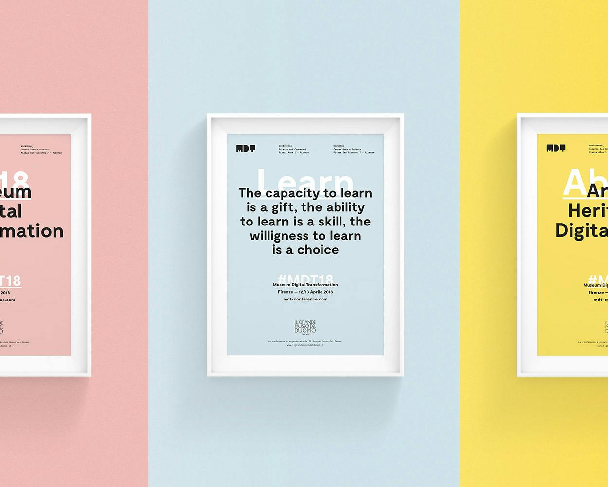 Tre cornici bianche con manifesti colorati sono appese su pareti di tonalità pastello: rosa, blu e gialla; il primo recita "Museum Digital Transformation 2018", il secondo contiene una citazione sull'importanza dell'apprendimento, e il terzo evidenzia "Arts & Heritage + Digital media".