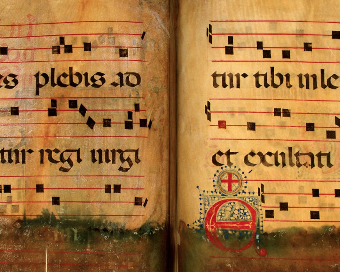 Un manoscritto antico aperto su due pagine contenente notazioni musicali medievali e testi in latino, con caratteri gotici neri su pergamena ingiallita.