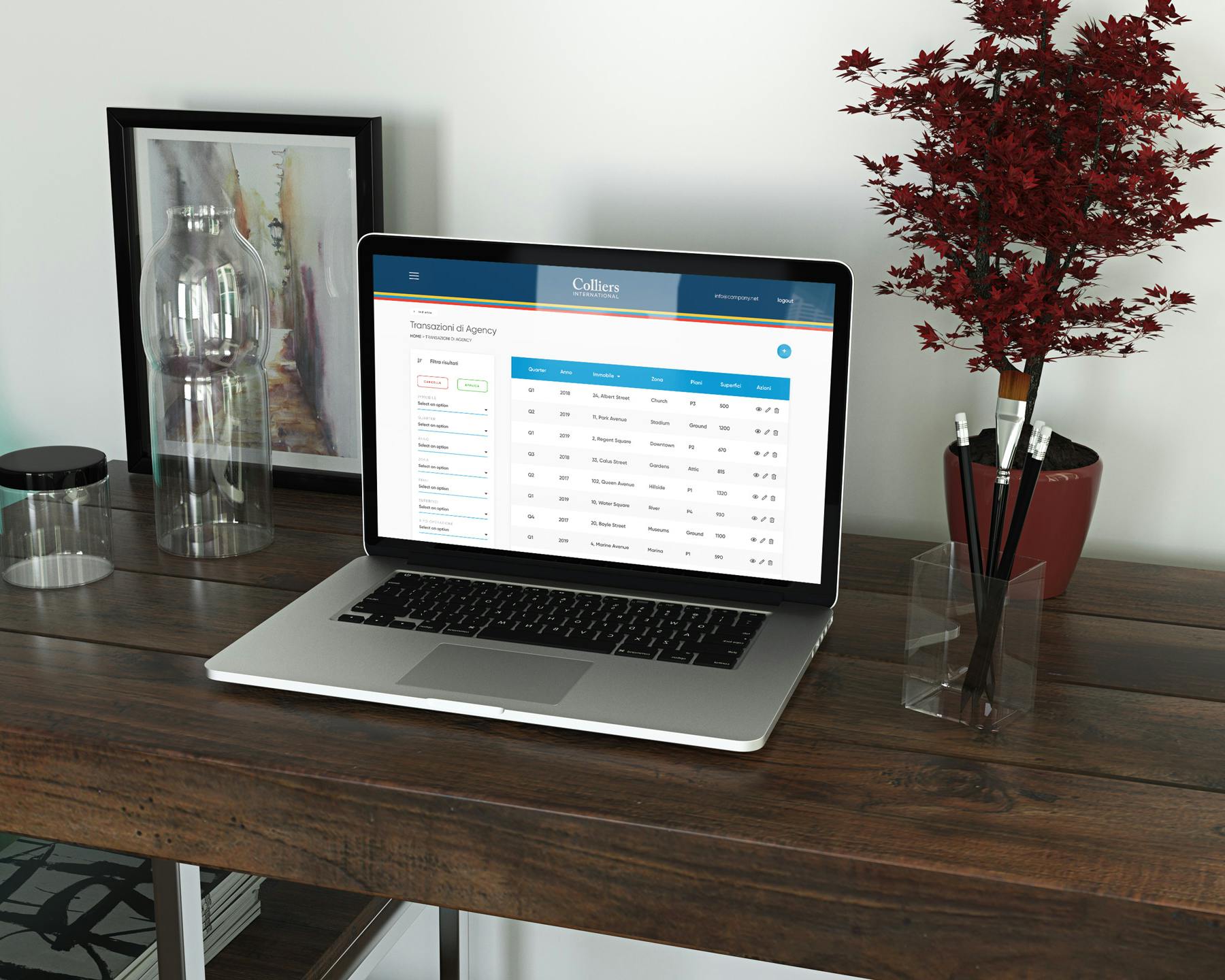 Un portatile aperto che mostra un'interfaccia di gestione delle fatture su un tavolo di legno scuro, accanto a decorazioni in vetro e una pianta rossa, riflettendo un ambiente di lavoro moderno e organizzato.