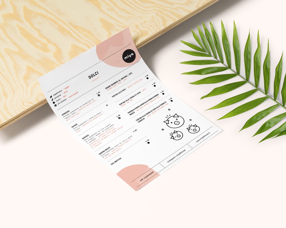 Immagine di un menu di dolci elegante su un tavolo di legno chiaro accanto a una foglia verde stilizzata, con dettagli grafici moderni in rosa e nero.