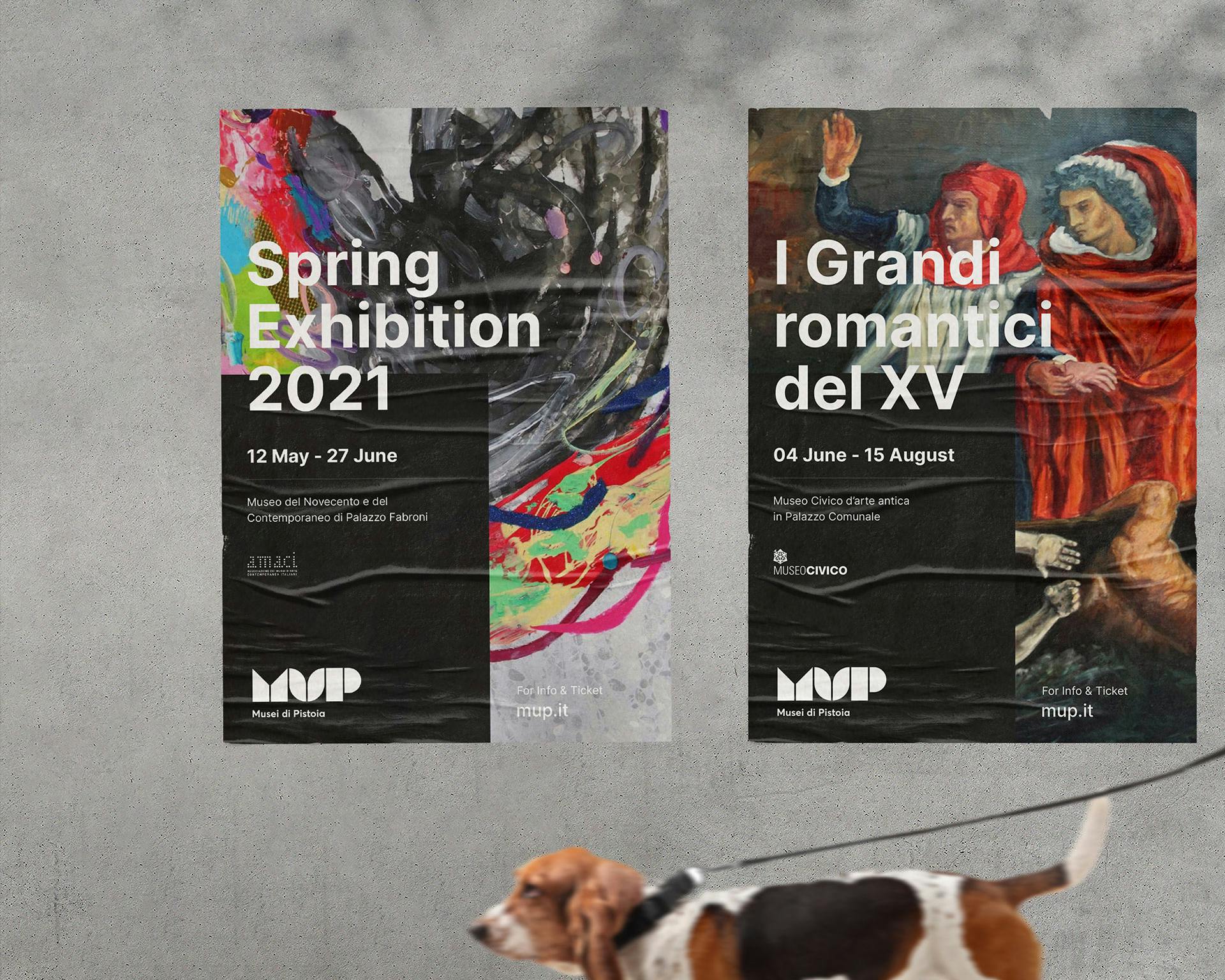 Un cane al guinzaglio passa davanti a due poster di una mostra; il primo poster, a sinistra, pubblicizza la "Spring Exhibition 2021" con colori astratti, mentre il secondo, a destra, promuove l'esposizione "I Grandi romantici del XV" con un dipinto storico.