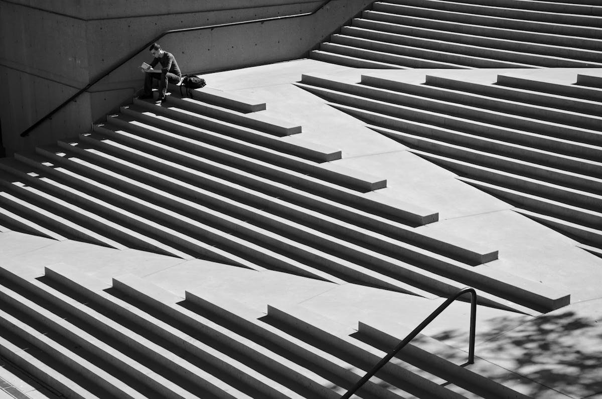 Foto in bianco e nero di un ragazzo che legge seduto in una struttura a scalinate