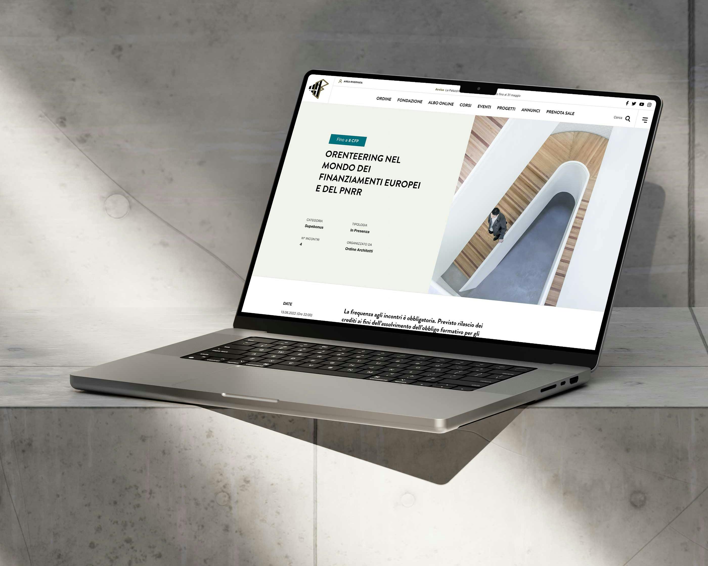 Un computer portatile moderno è appoggiato su una superficie in cemento, mostrando uno schermo con una pagina web che presenta uno scorcio architettonico, in un ambiente ben illuminato.