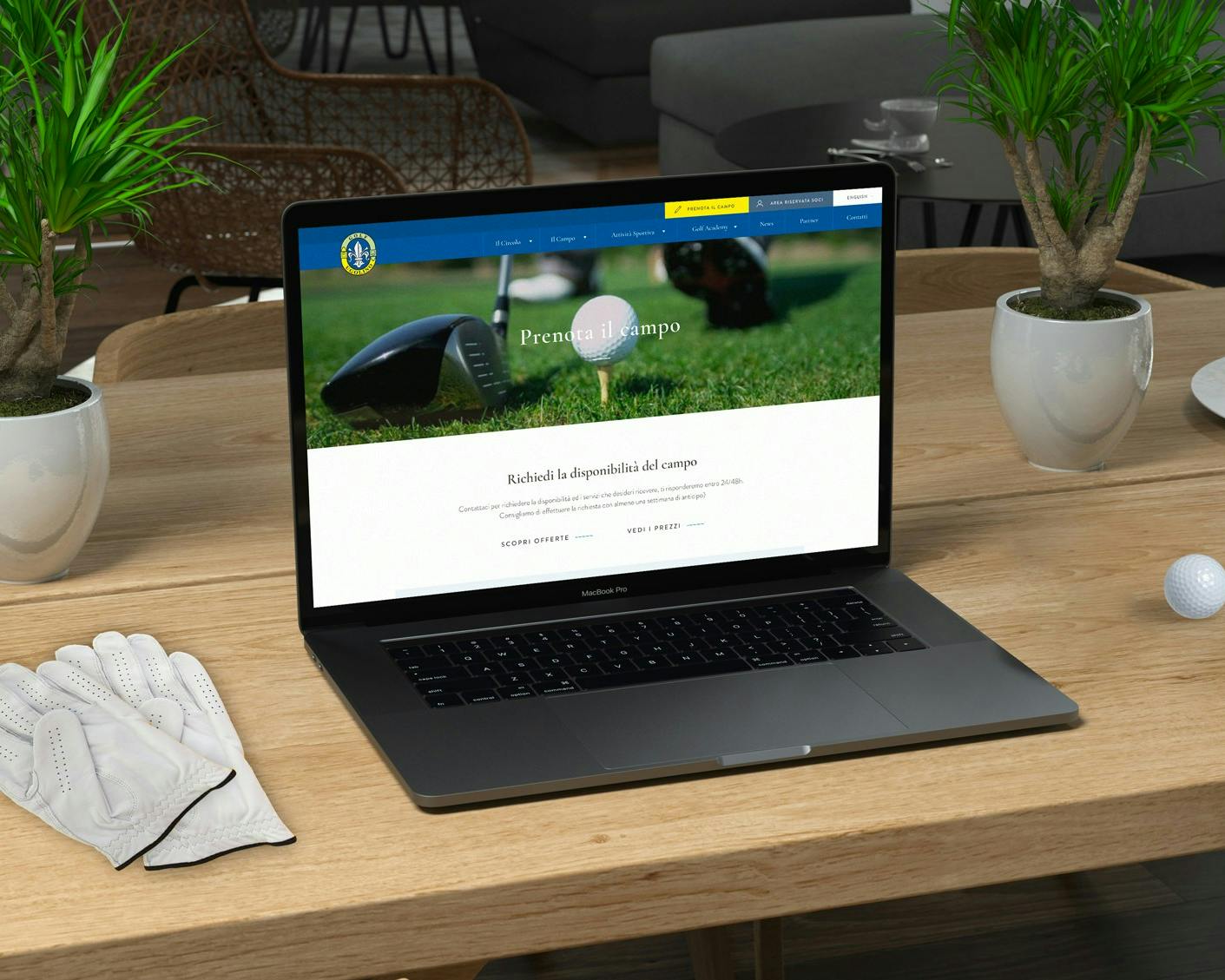 Un laptop aperto su un sito di golf è appoggiato su un tavolo di legno, circondato da guanti da golf bianchi, una palla da golf e due piantine in vaso.
