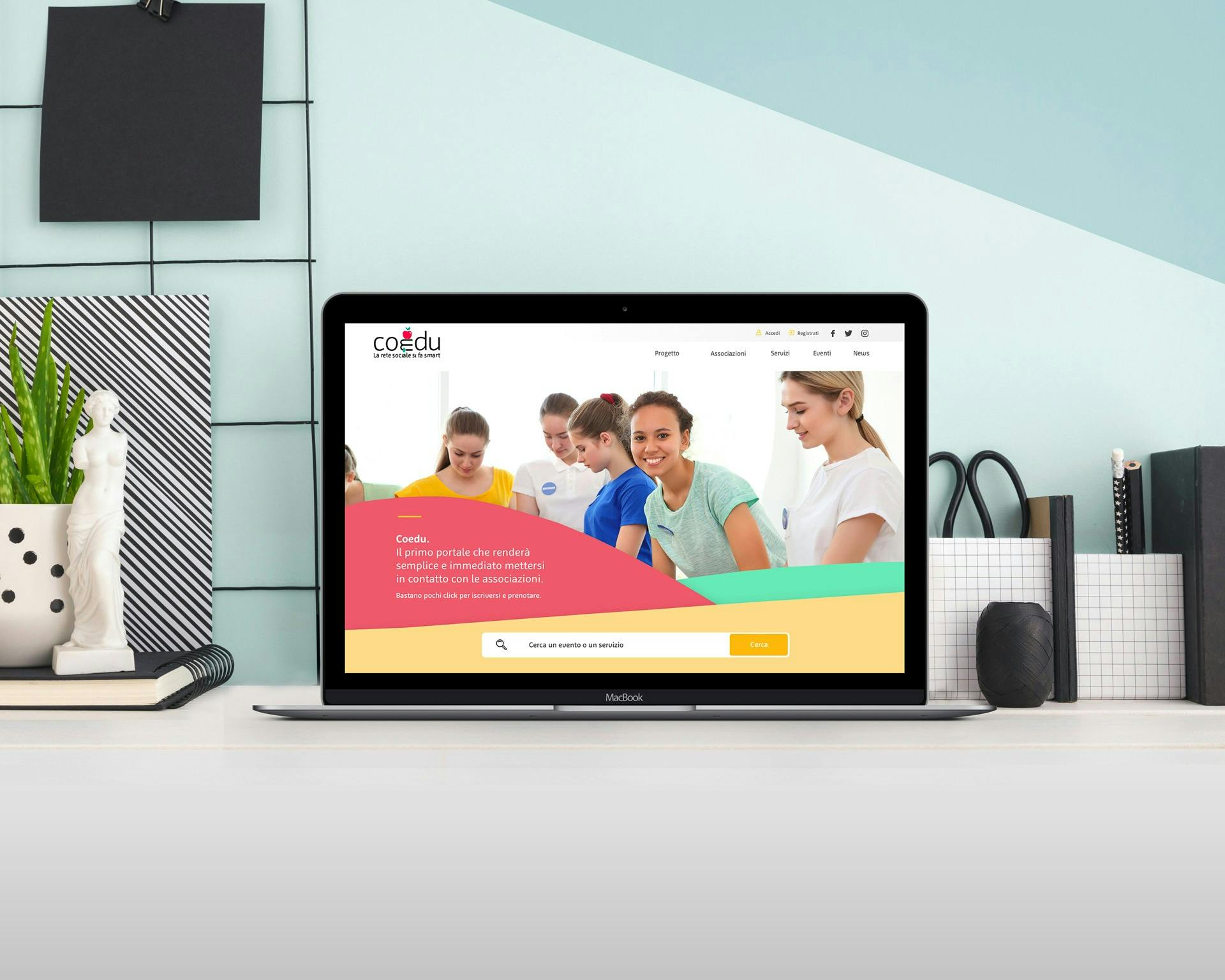 Un laptop aperto mostra una pagina web con un gruppo di persone che sorridono e lavorano insieme, posizionato su una scrivania moderna decorata con libri, una pianta e oggetti di cancelleria, ideale per concetti di lavoro collaborativo e spazio di lavoro elegante.