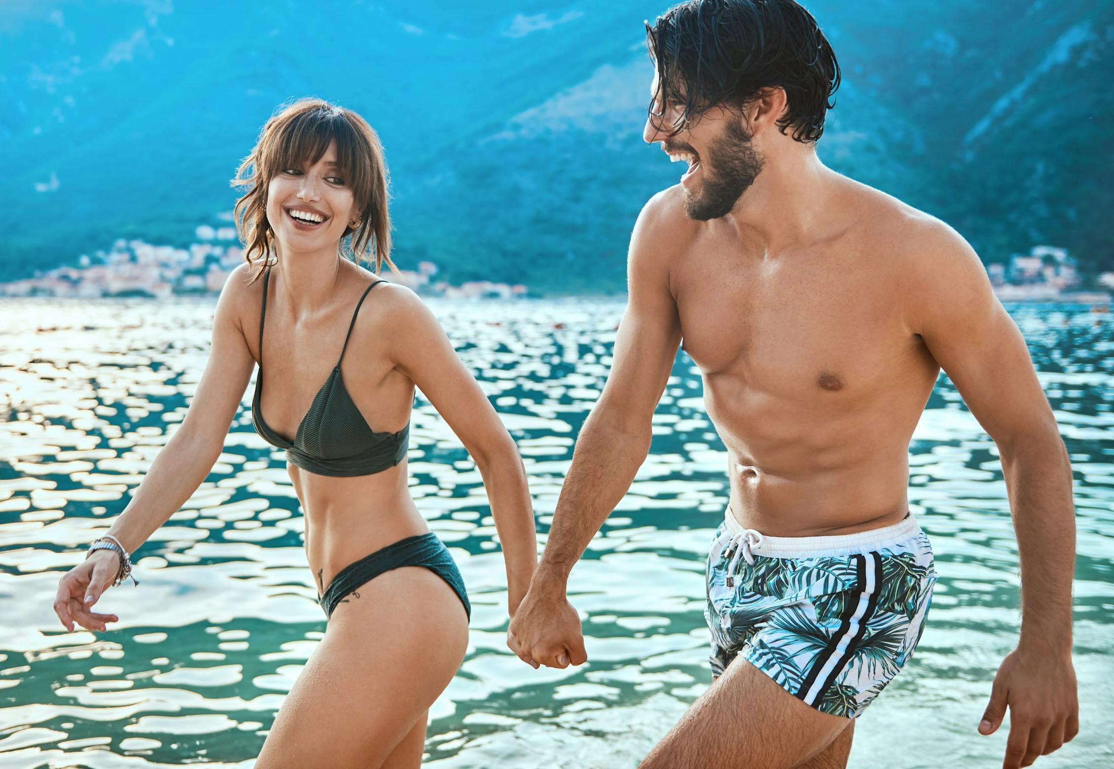 Man and woman walking in the water at the ocean wearing bathing suits