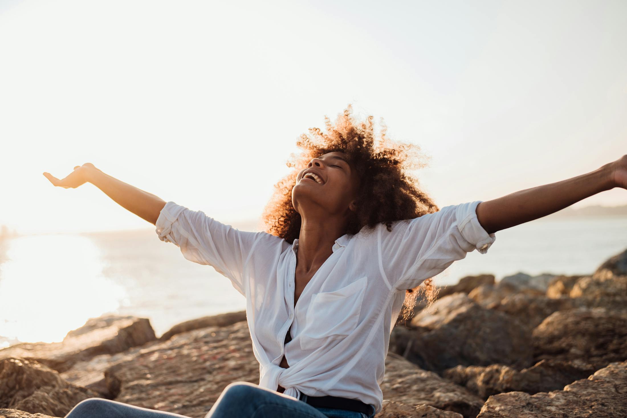 Woman at the beach with her arms stretched to the site while looking up and smiling