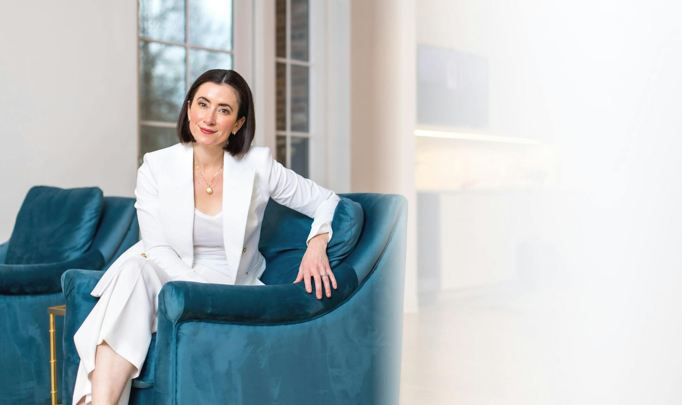 Dr. Helen Moses in white shirt and blazer posing on blue couch