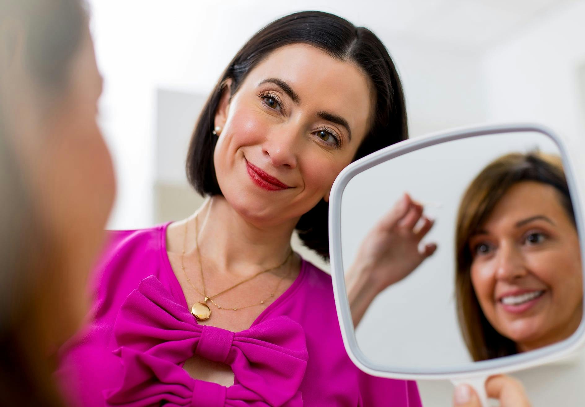Smiling woman looking at face in mirror with Dr. Helen Moses