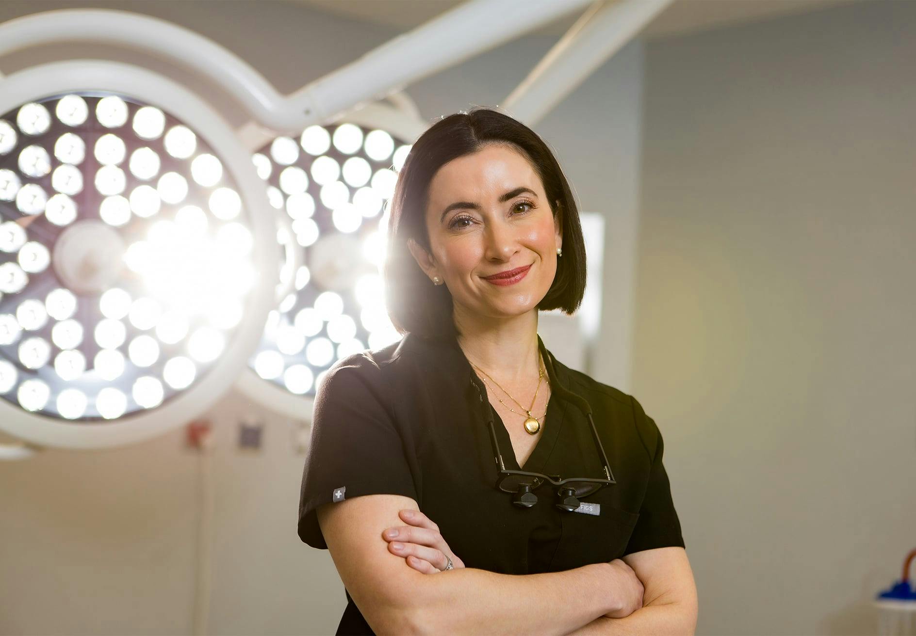 Dr. Helen Moses standing in front of operating lights in a black scrubs shirt