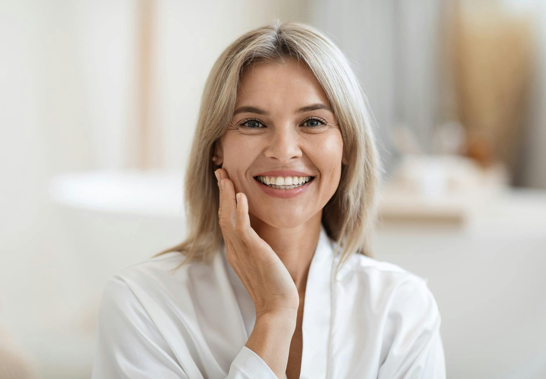 smiling woman in white shirt touching face