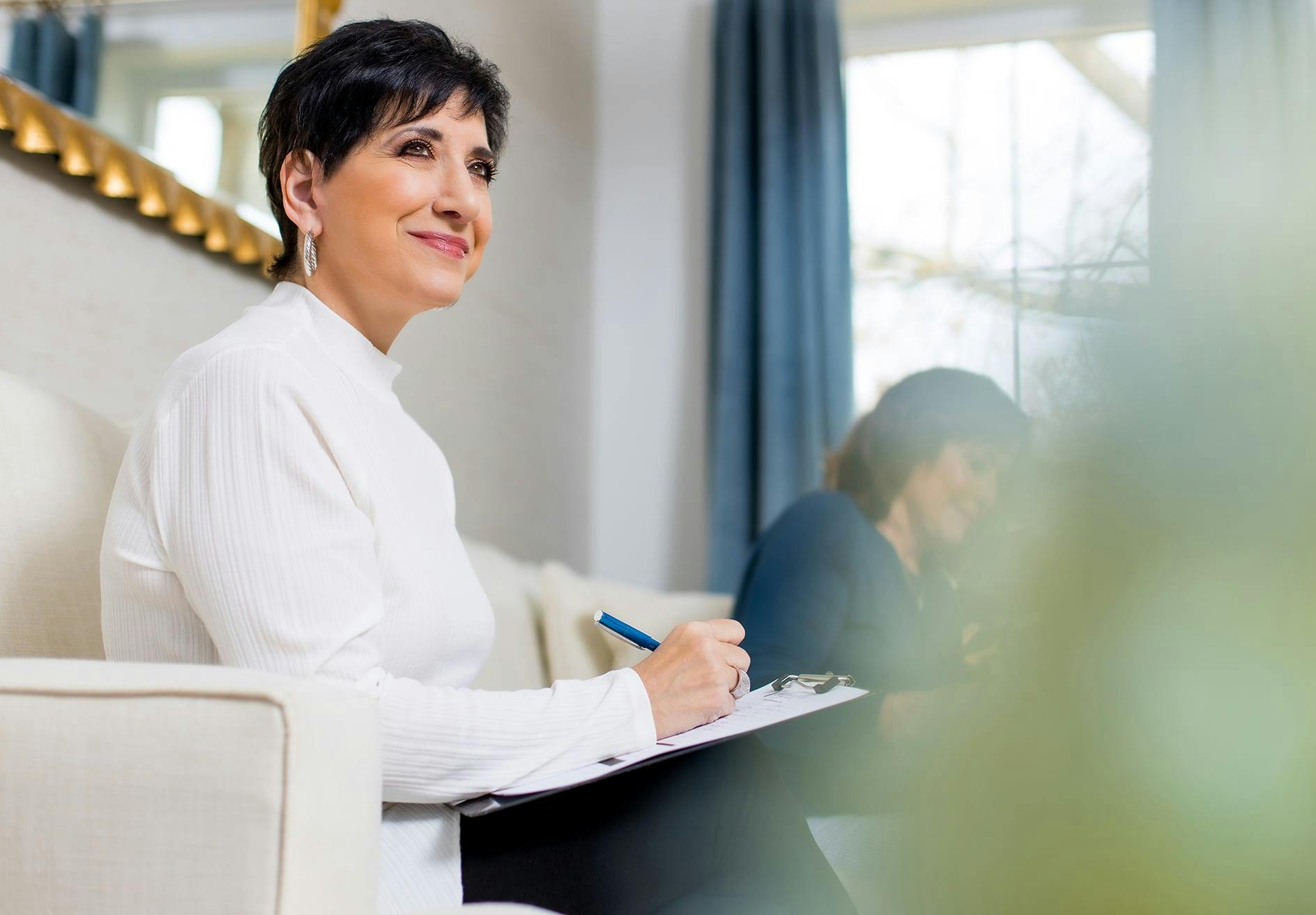 smiling woman sitting on a couch with a notebook and pen
