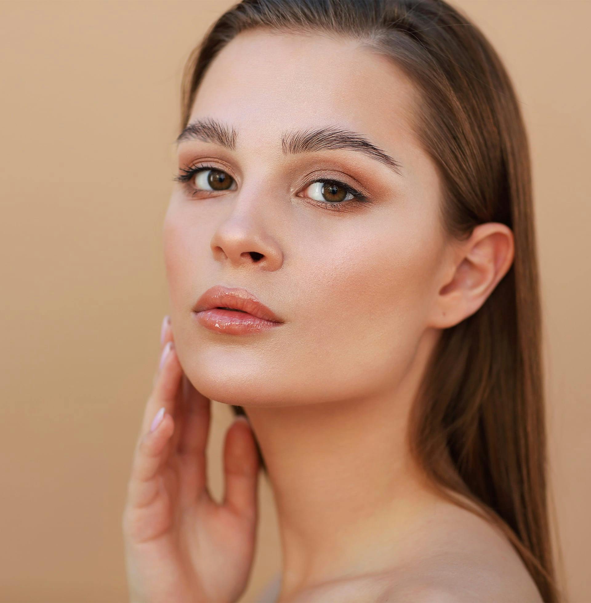 close up of woman against yellow background touching her face