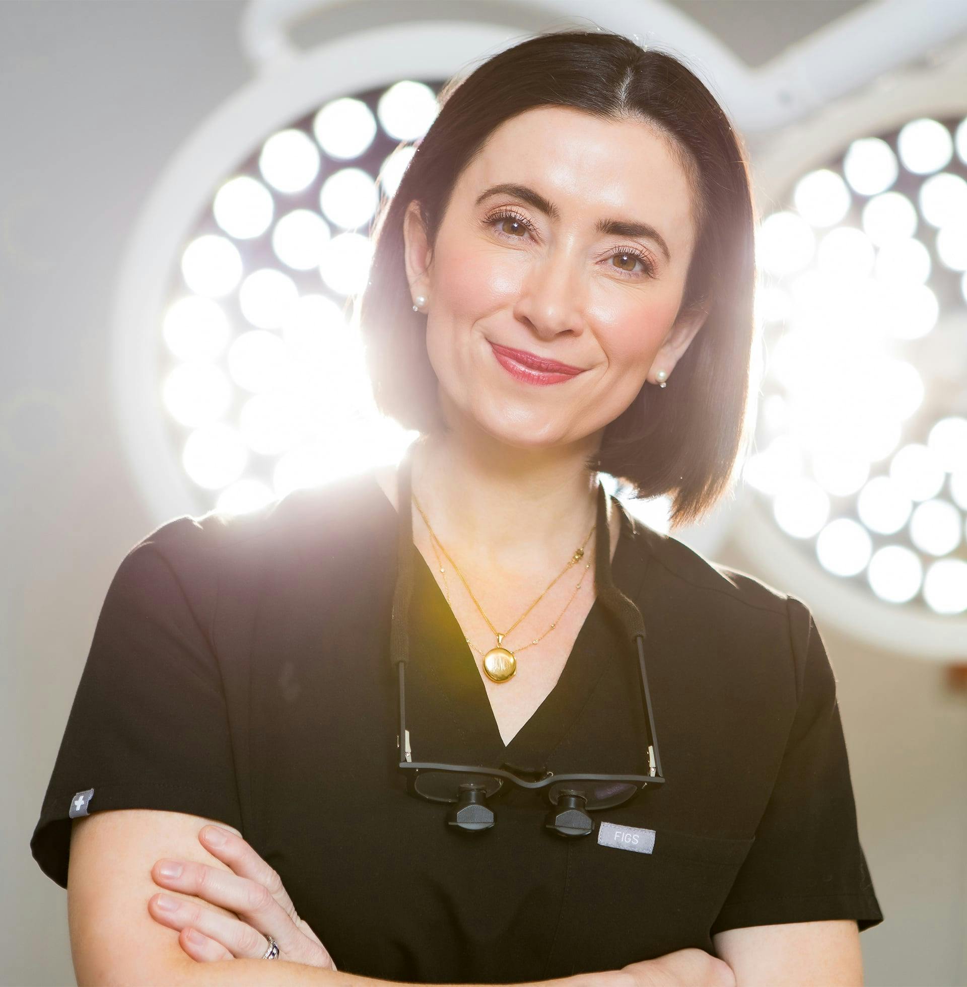 smiling Dr. Helen Moses in black shirt standing in front of operating lights