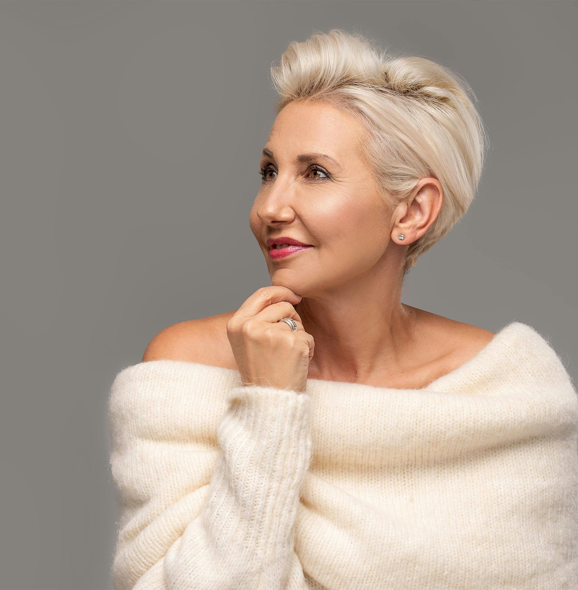 blond woman with short hair wearing a white fur sweater and posing for a picture