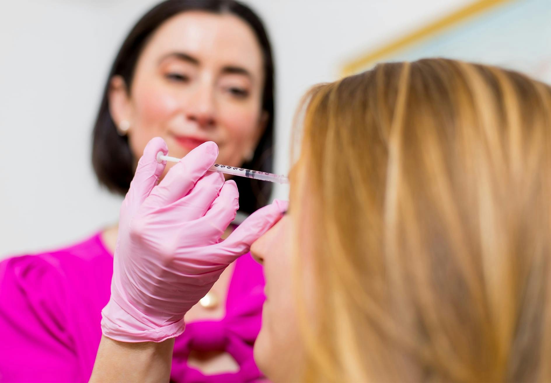 Dr. Helen Moses in pink shirt and gloves holding a syringe to woman's face