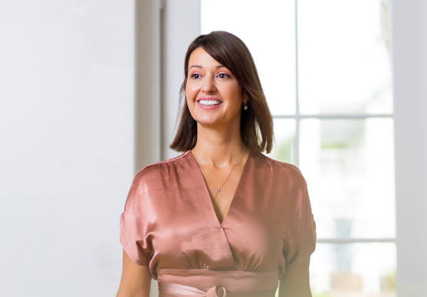 smiling woman in a pink dress standing in front of a window
