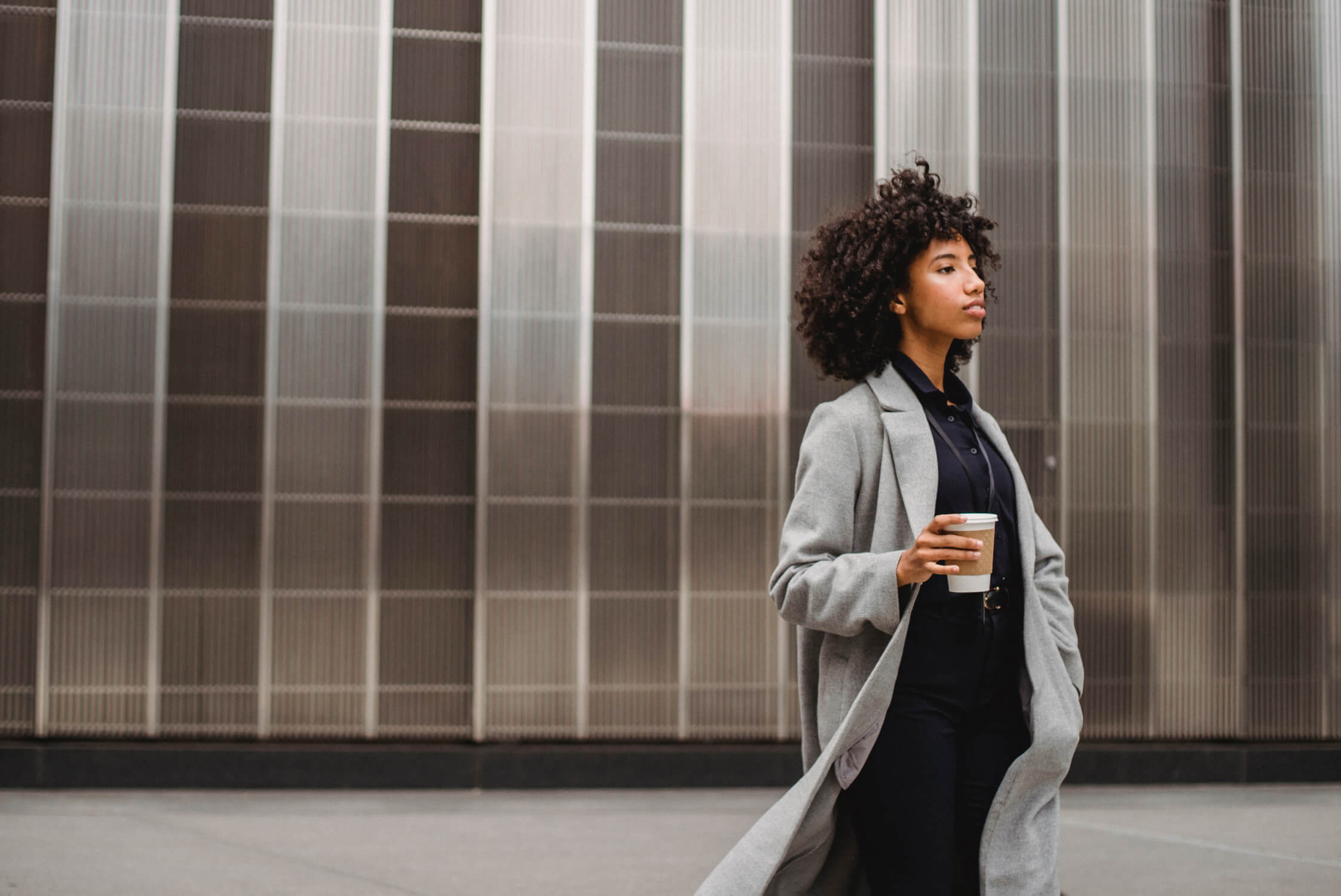 Una donna cammina per strada con un caffè in mano e lo sguardo pensieroso
