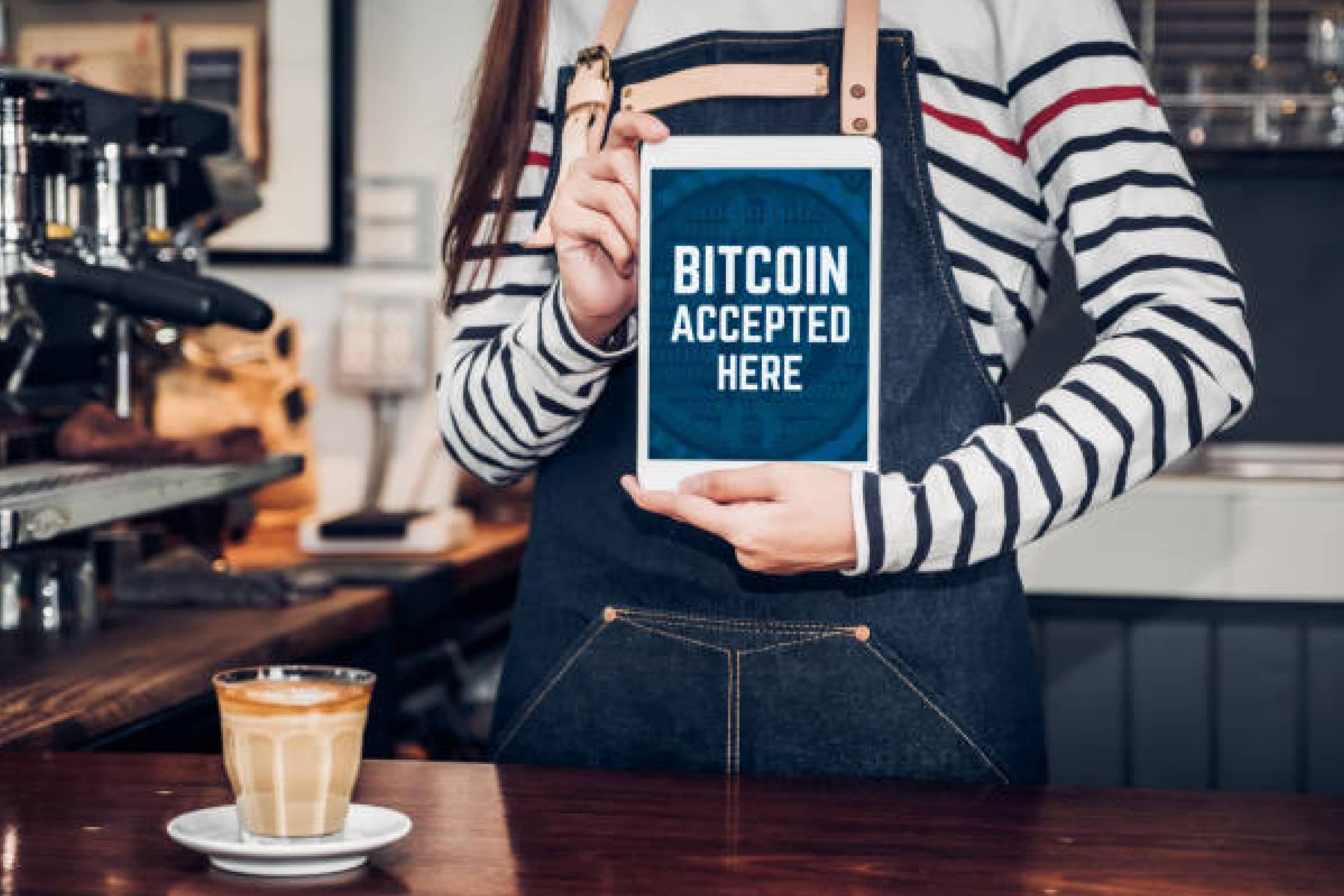 Eine Barista hält ein Schild hoch, dass Bitcoins akzeptiert sind