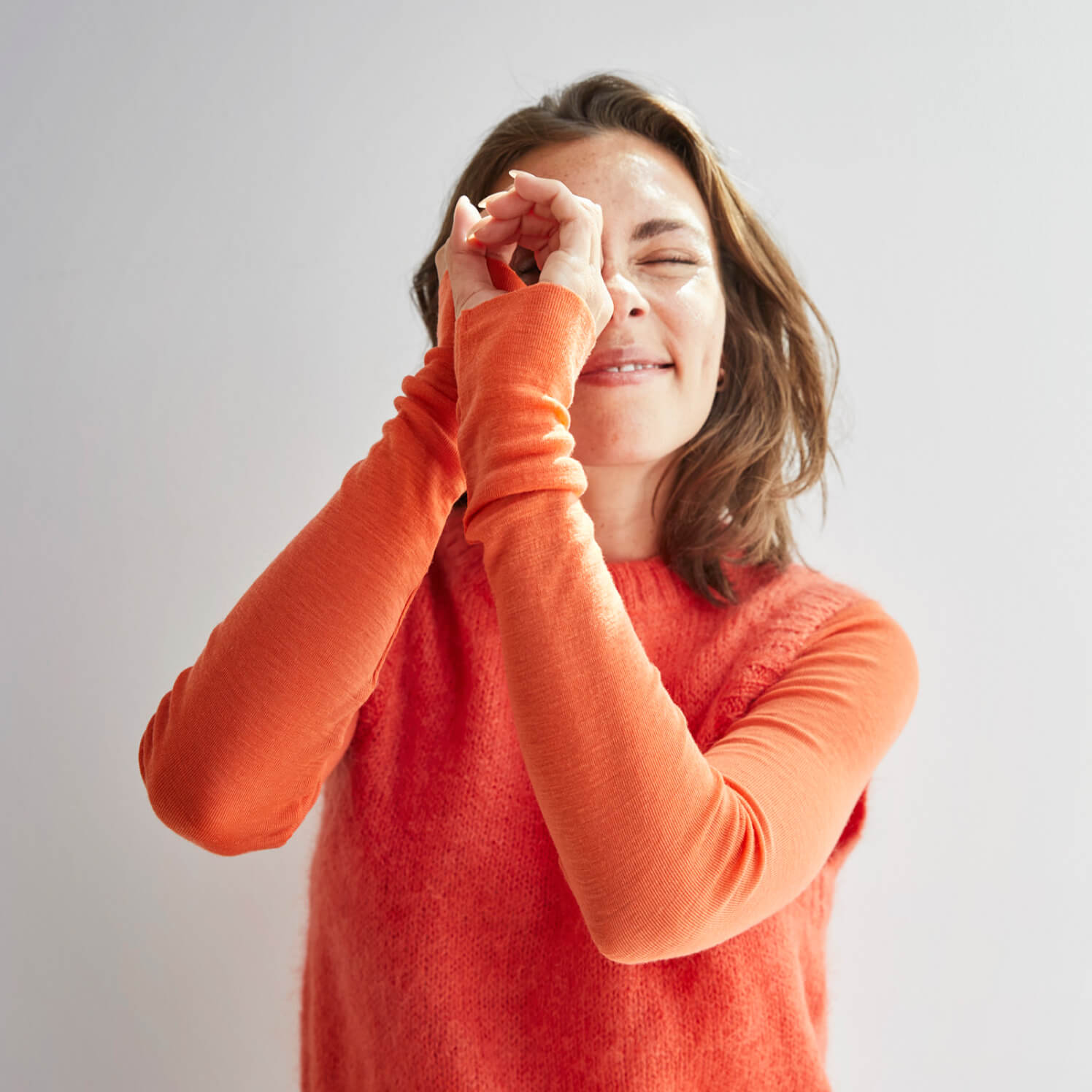 Une femme en pull orange utilise ses mains comme des jumelles et regarde symboliquement vers l'avenir