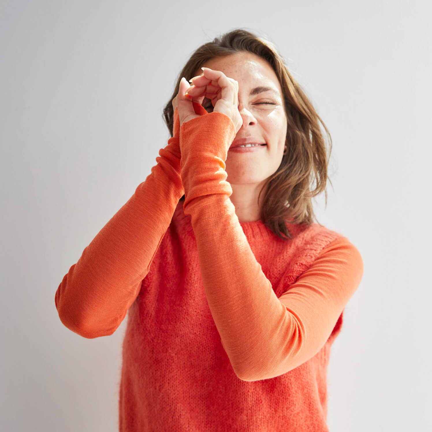 A woman in an orange sweater uses her hands as binoculars and symbolically looks into the future