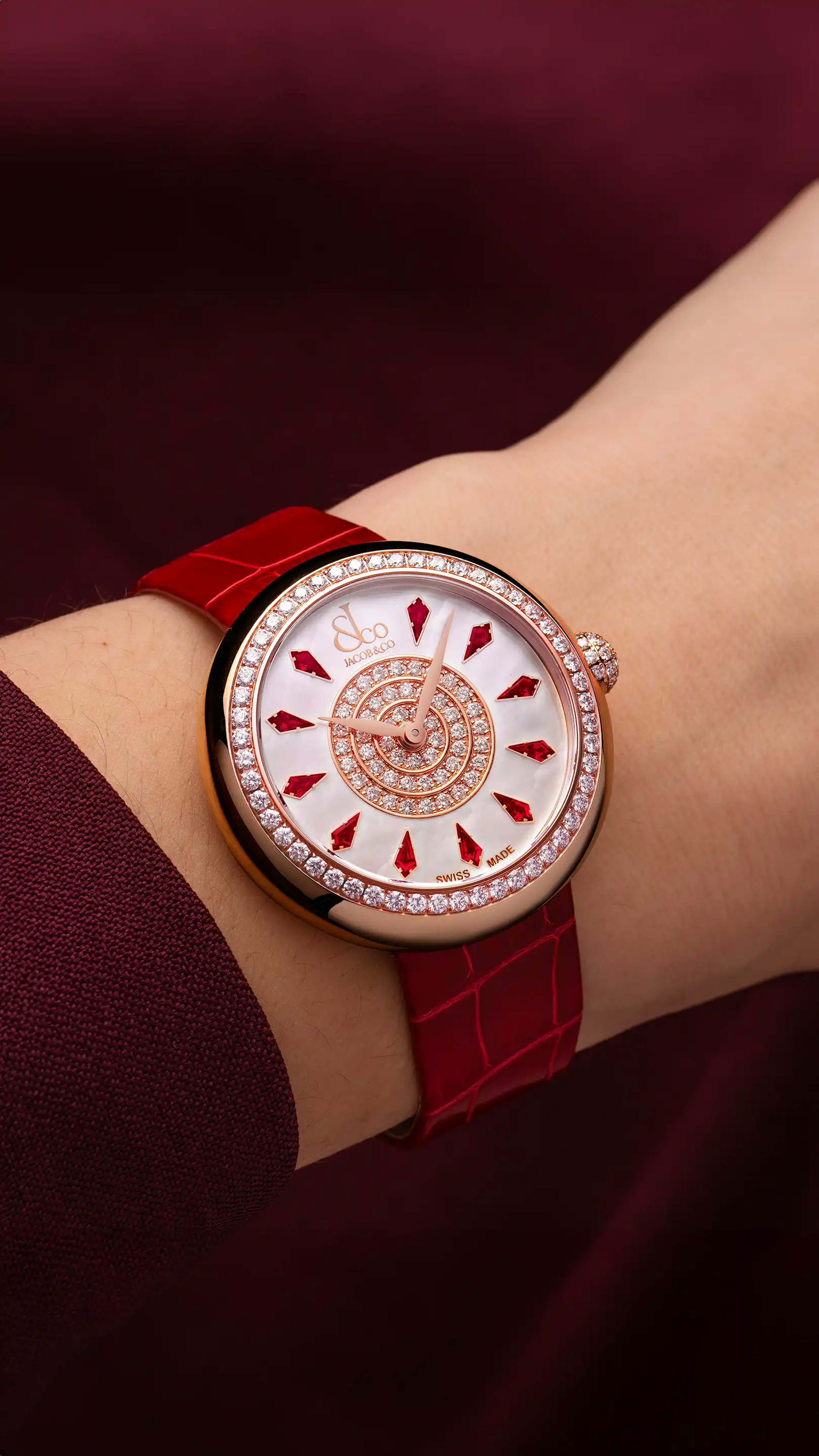 The rose gold, red Brilliant Watch, with ruby hour markers. Worn on the left wrist.