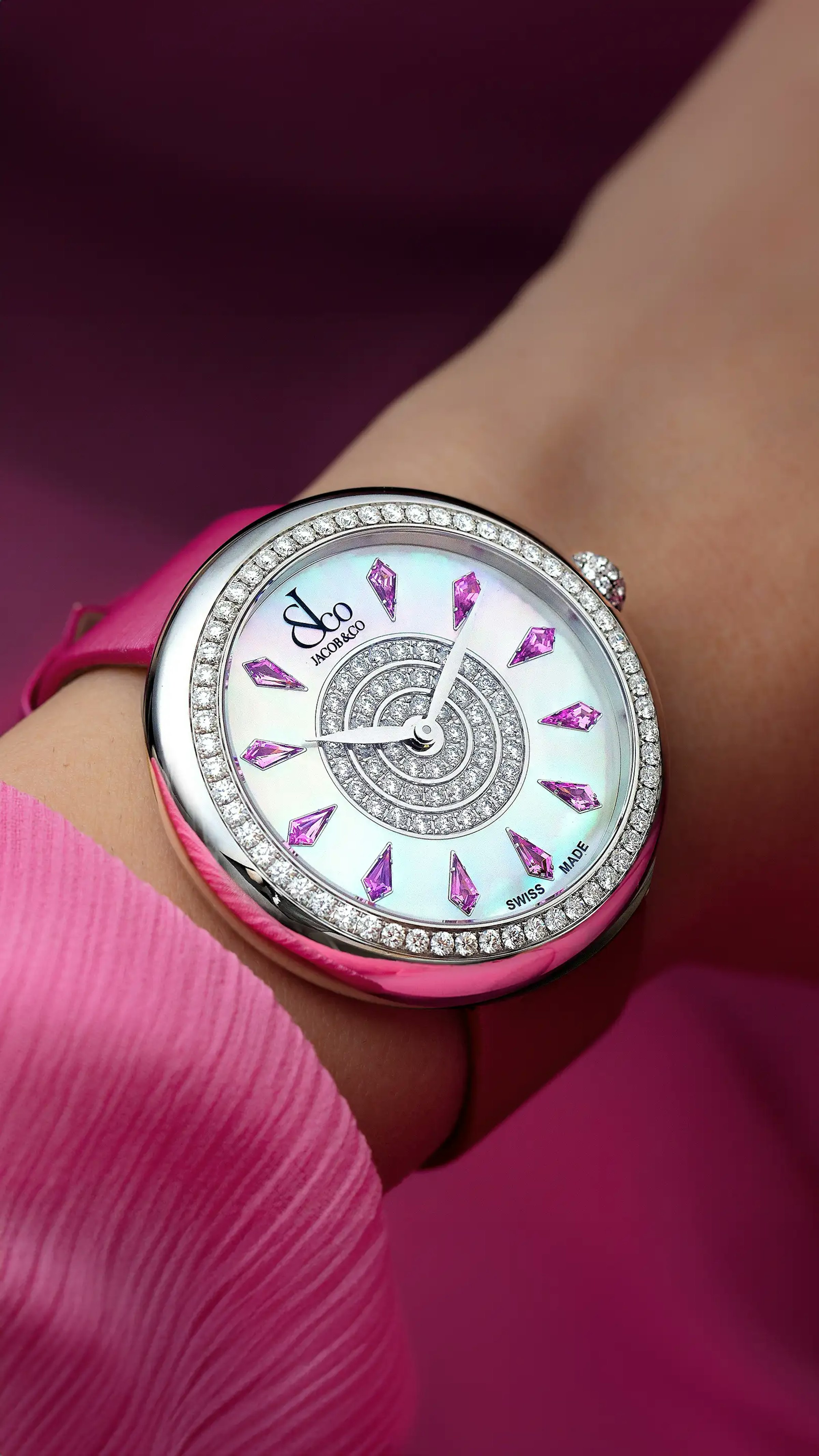 The stainless steel, pink Brilliant Watch, with pink sapphire hour markers. Worn on the left wrist.
