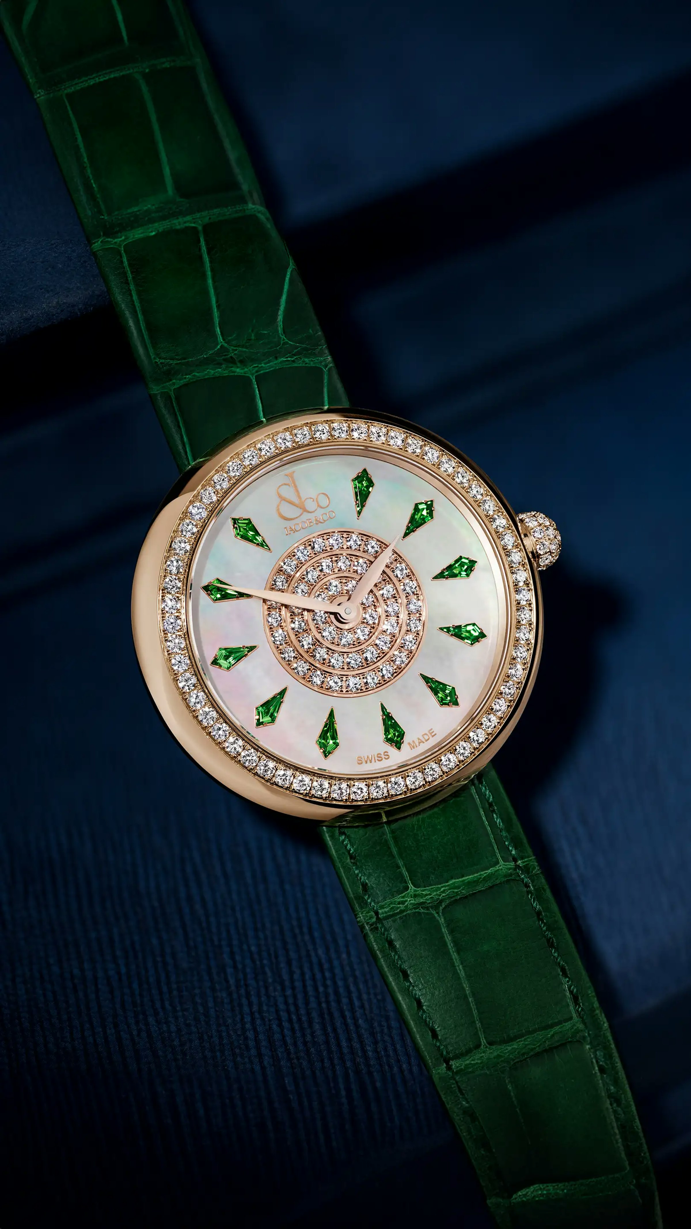 The rose gold, tsavorite Brilliant Watch, with tsavorite hour markers. Laid flat on a surface.