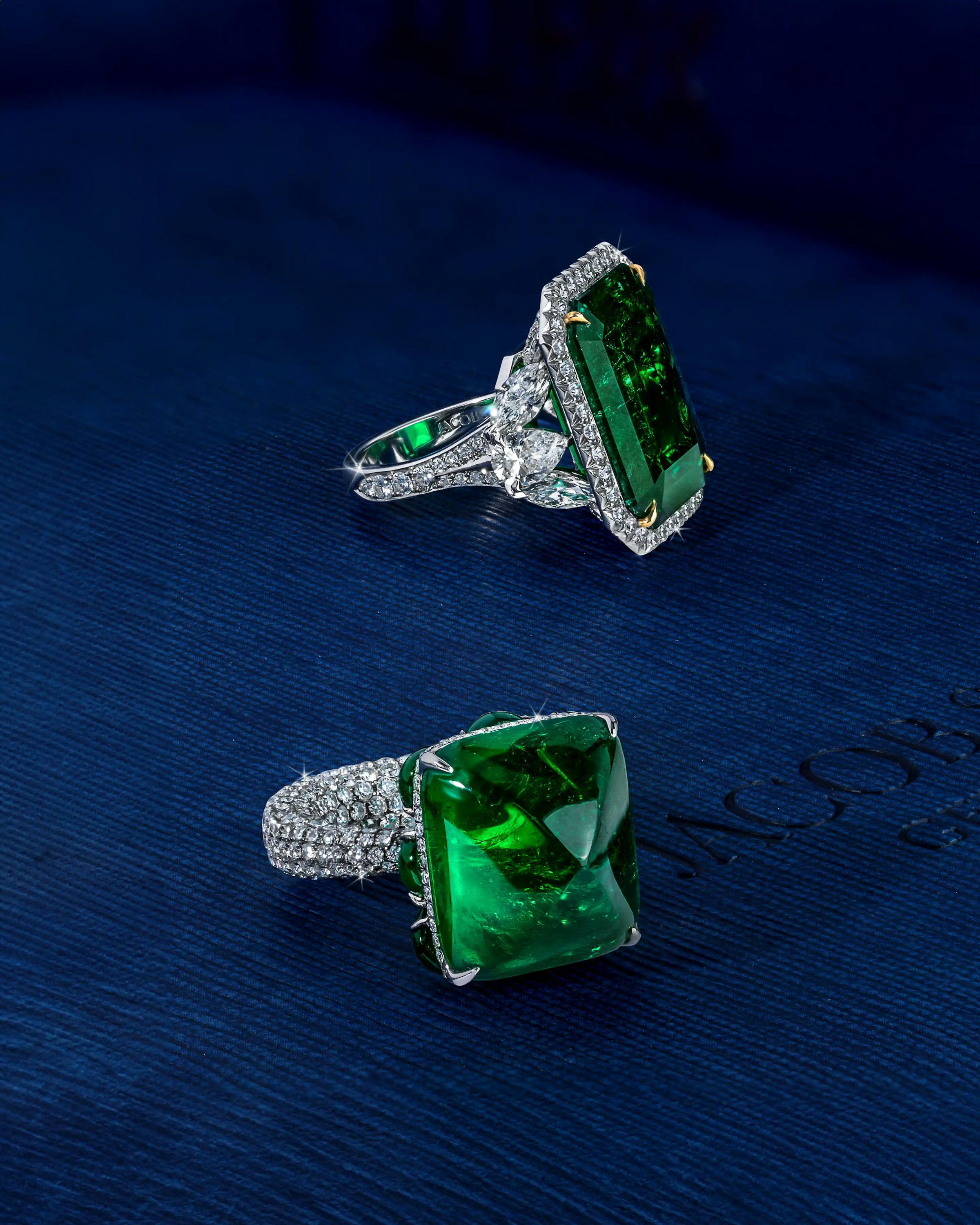 the ring, alongside another emerald ring, laid flat on a surface