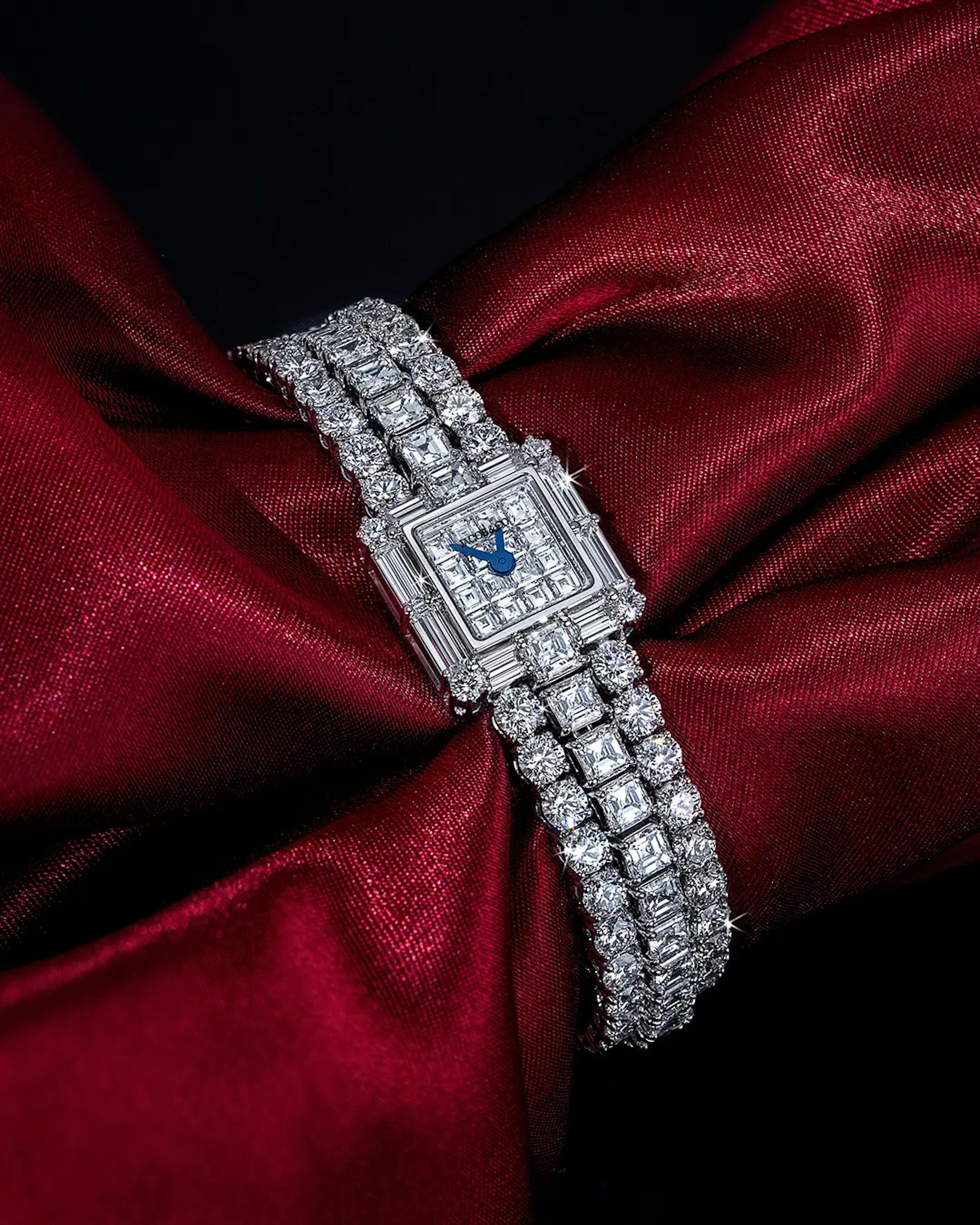 An image of a diamond watch anklet laid on a dark read silk fabric.