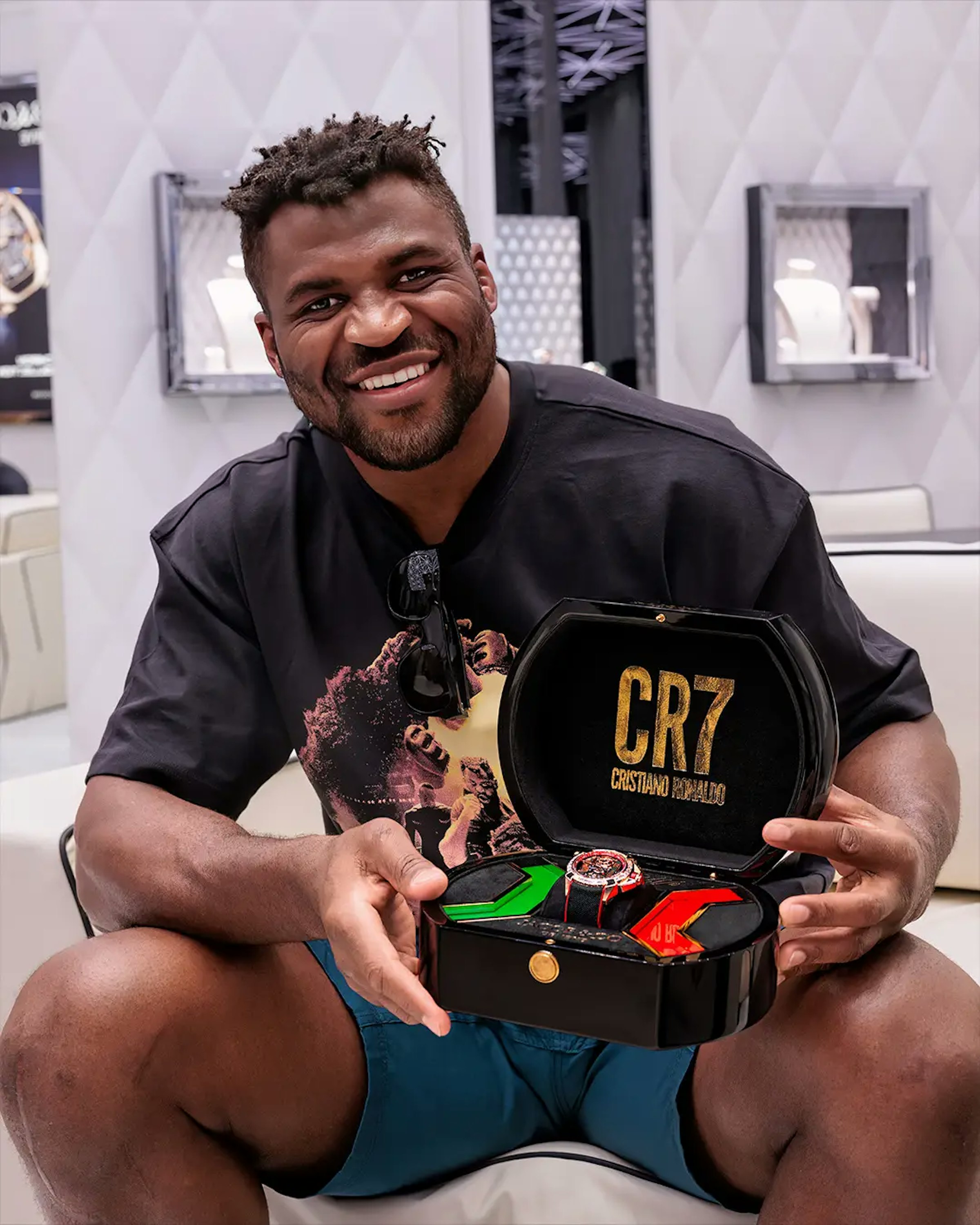Image of a man sitting on a chair and holding an opened watch box withCR7 written on the lid and a watch in the middle