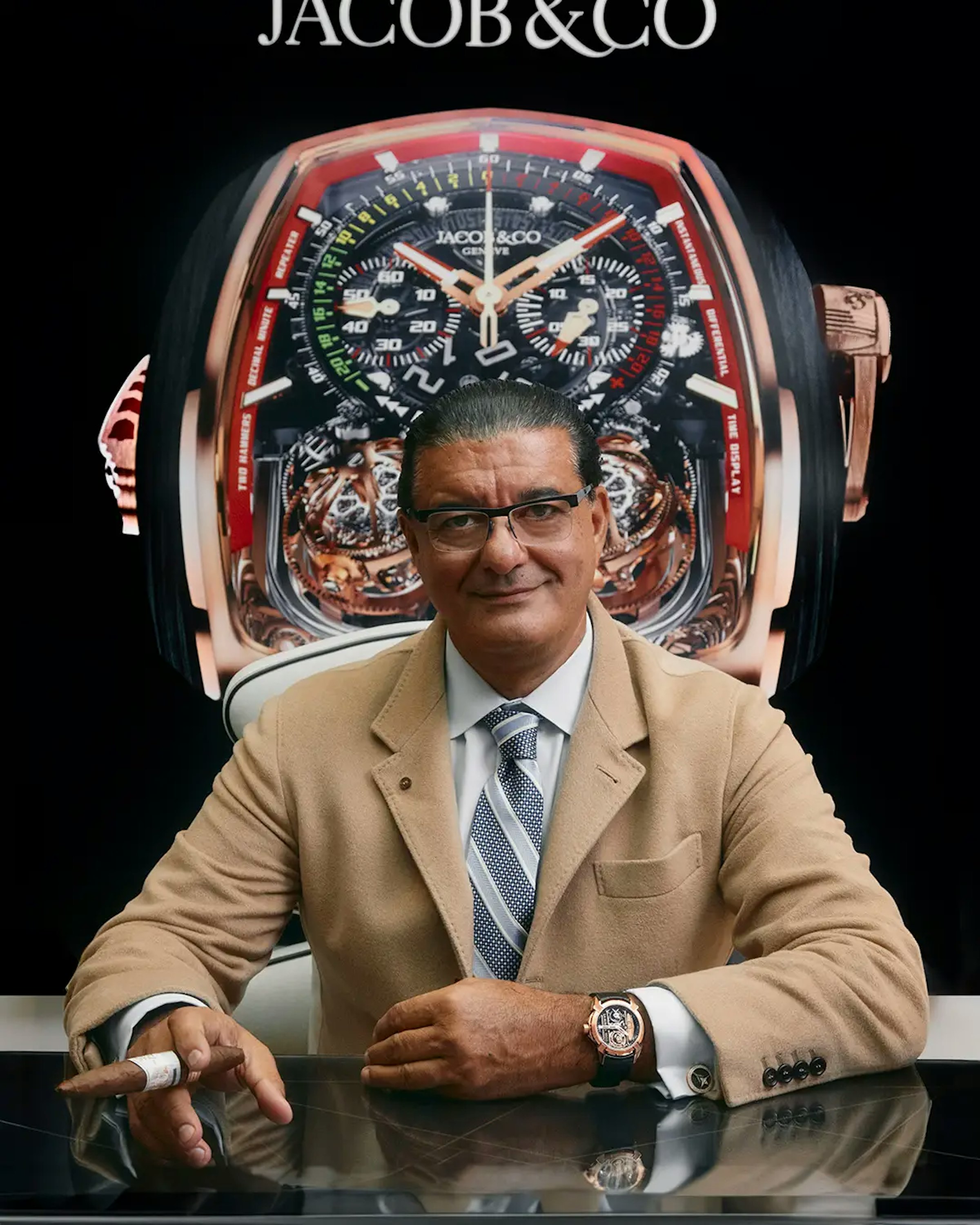 An image of Jacob Arabo sitting behind the desk wearing the Epic X La Aurora watch and holding a cigar on his right hand