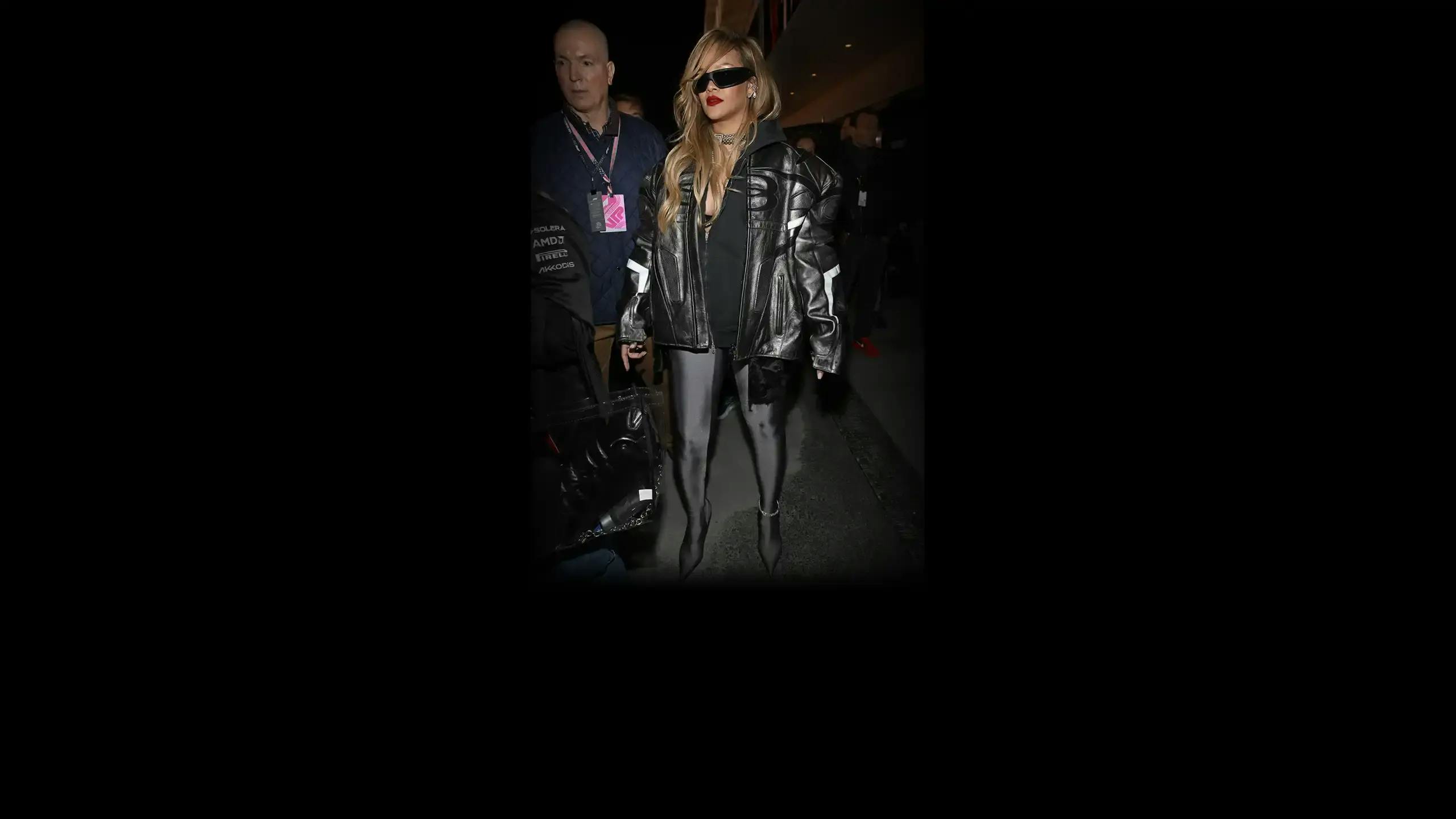 A full body image of Rihanna wearing an all black outfit with a watch anklet on her left ankle.