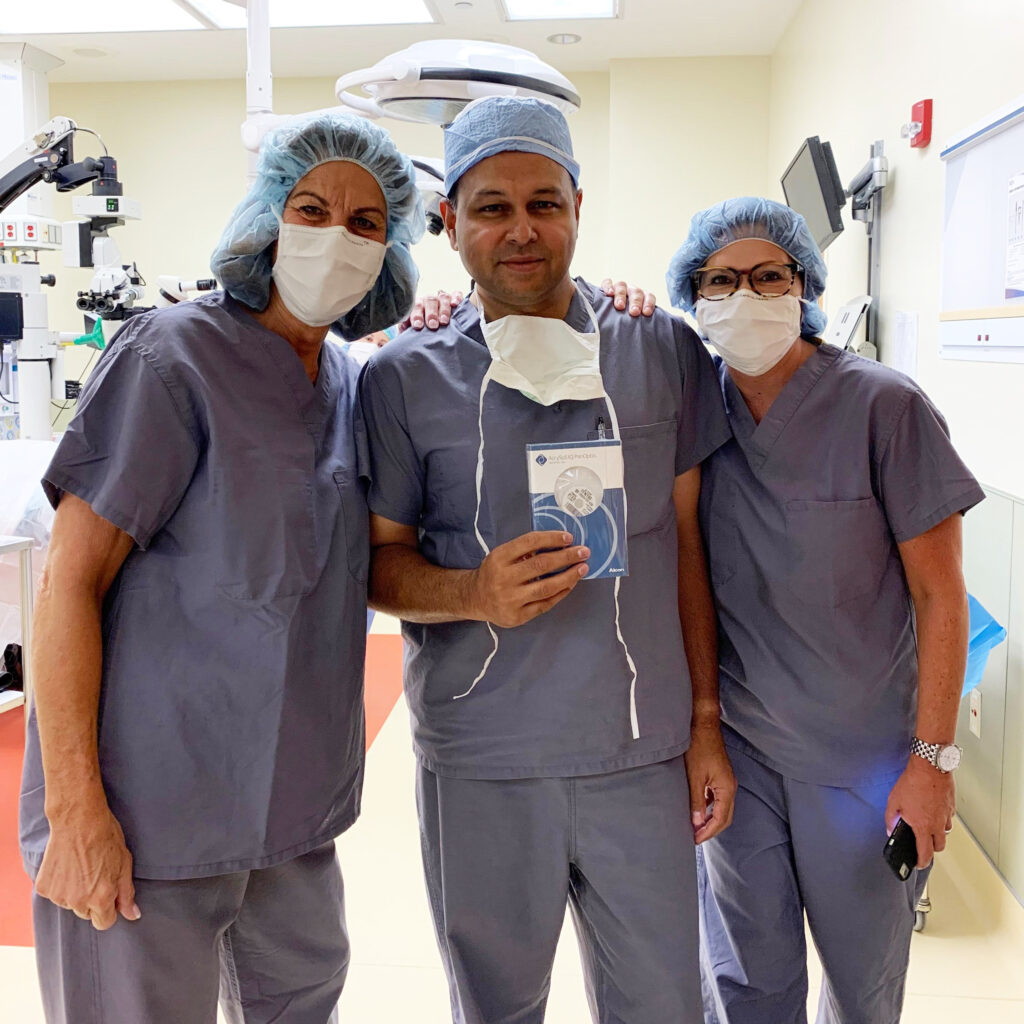 Three doctors in cataract surgery room, one holding the PanOptix trifocal intraocular lens.