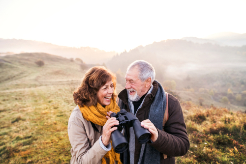 husband and wife in a field holding binoculars