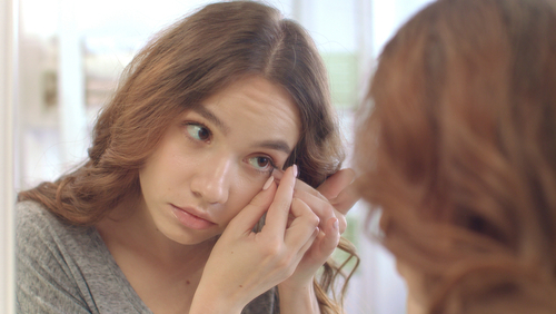 woman looking into mirror as she puts in contacts 