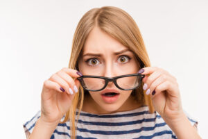 woman looking through glasses that she is holding in front of her face